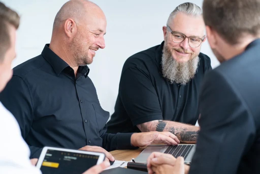 Ein Team von Kollegen diskutiert bei einem Meeting und tauscht Ideen am Tisch aus, mit Laptops und Notizbüchern.