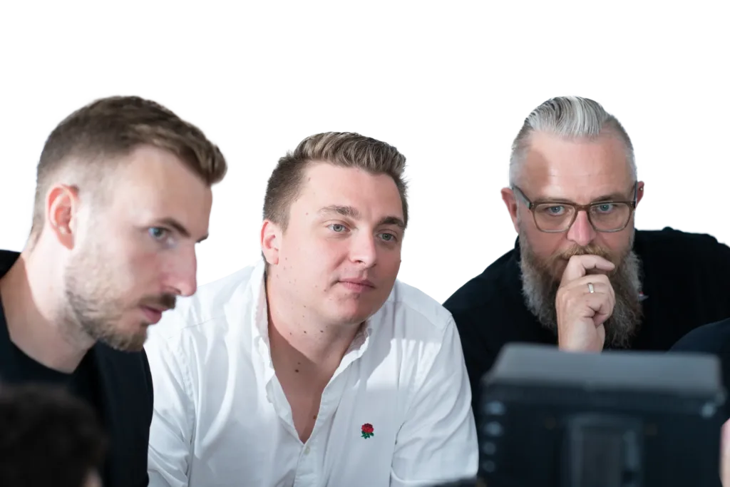 Drei Kollegen arbeiten konzentriert gemeinsam an einer Aufgabe, während sie auf einen Bildschirm schauen.