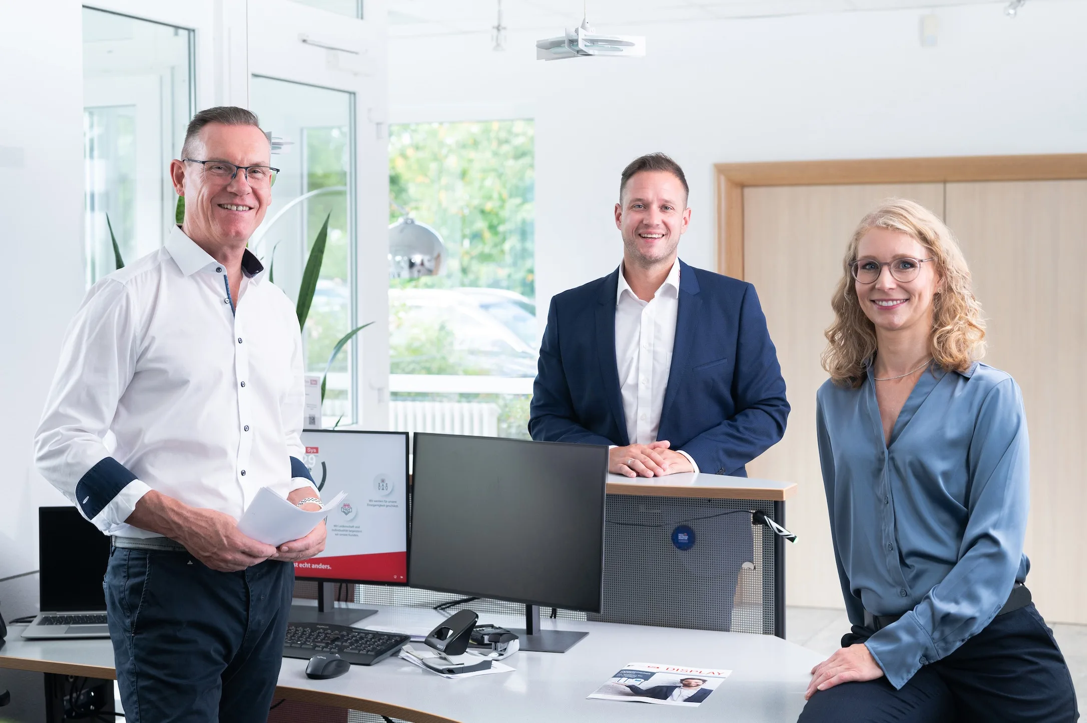 Achim Geus, Matthias Müller und Katharina Schmaus in einem modernen Büro, die lächelnd in die Kamera schauen.