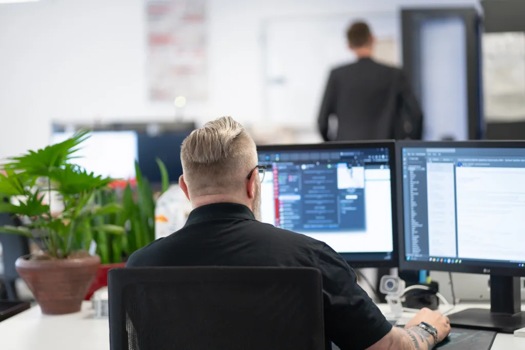 Eine Person arbeitet konzentriert an zwei Monitoren im Büro.