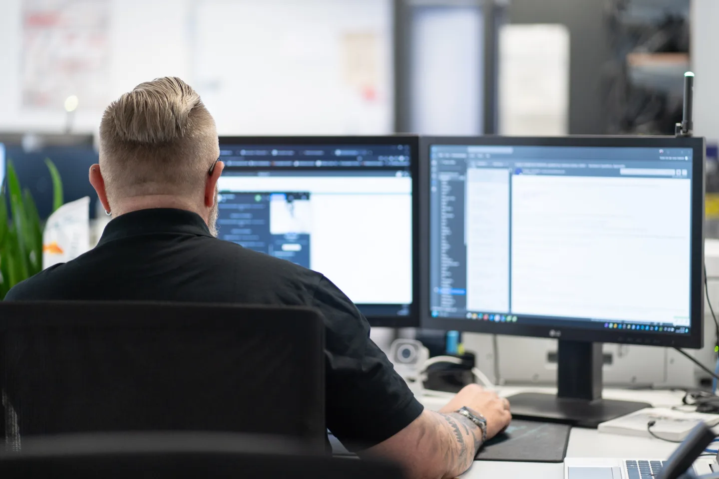 Ein Mitarbeiter arbeitet mit zwei Bildschirmen im Büro und konzentriert sich auf seine Aufgaben.