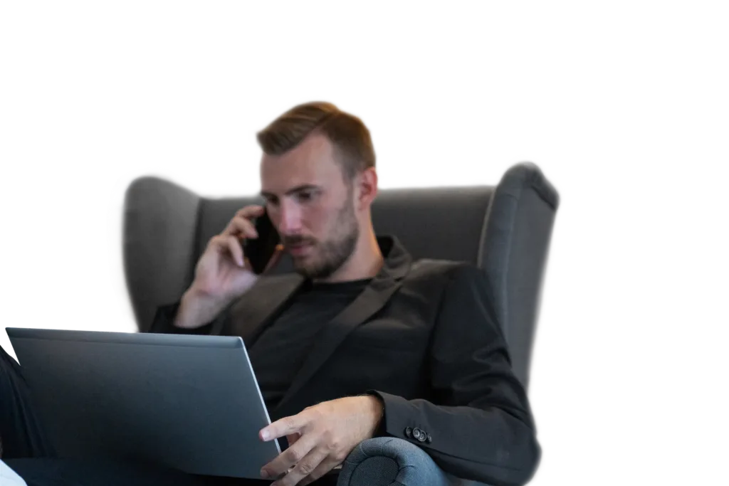 Eine Person sitzt in einem Sessel, arbeitet am Laptop und telefoniert in einem Remote-Setup.