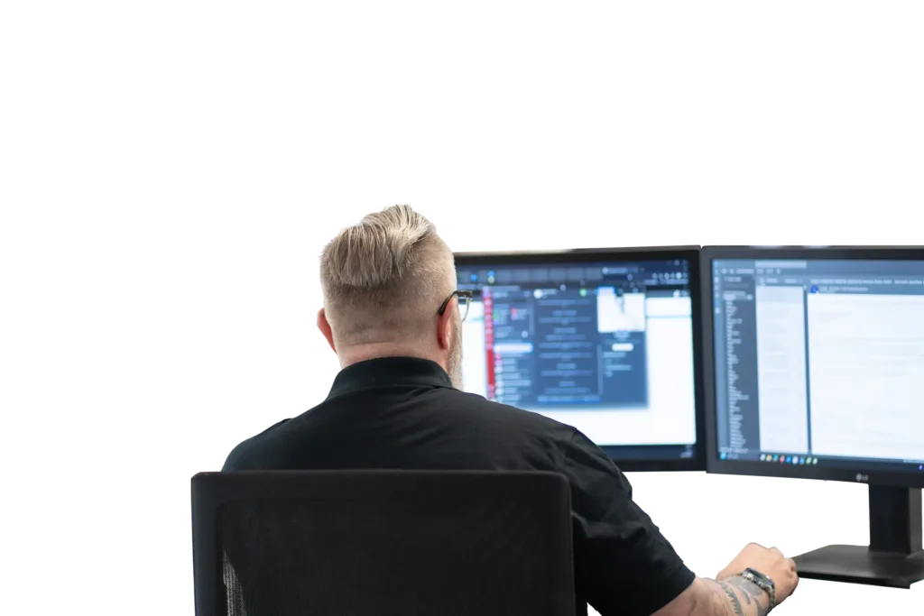 Eine Person arbeitet konzentriert an zwei Monitoren im Büro.