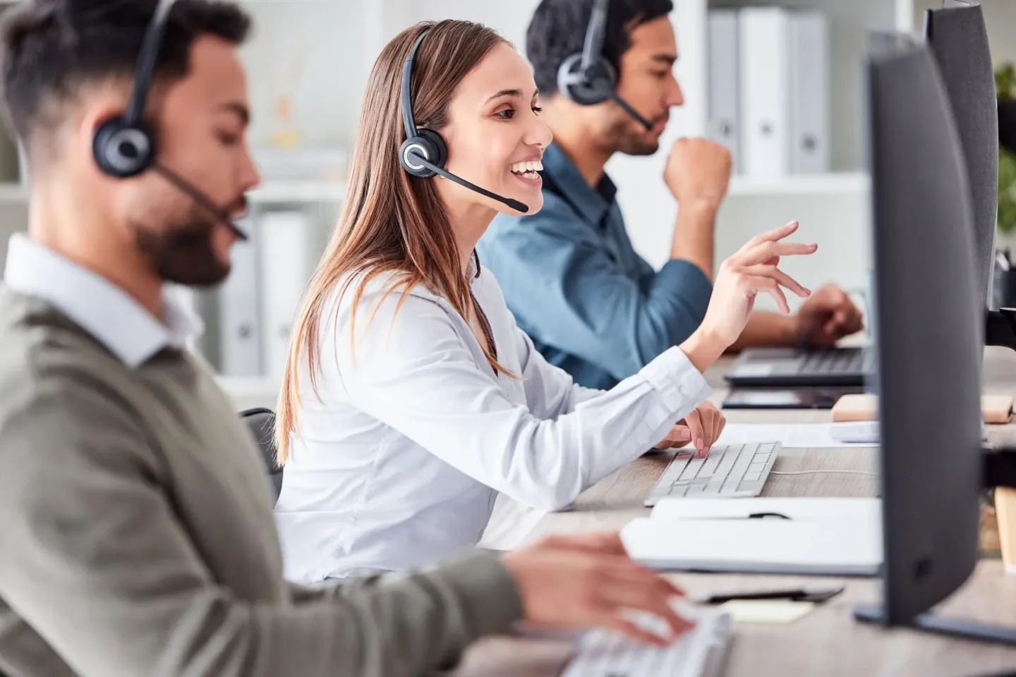 Zwei Männer und eine Frau arbeiten mit Headsets am Computer für das Contact Center und sind im Kundengespräch.