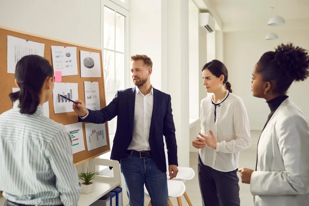 Vier Mitarbeiter besprechen an einer Tafel die Arbeitsschritte und betrachten Diagramme.