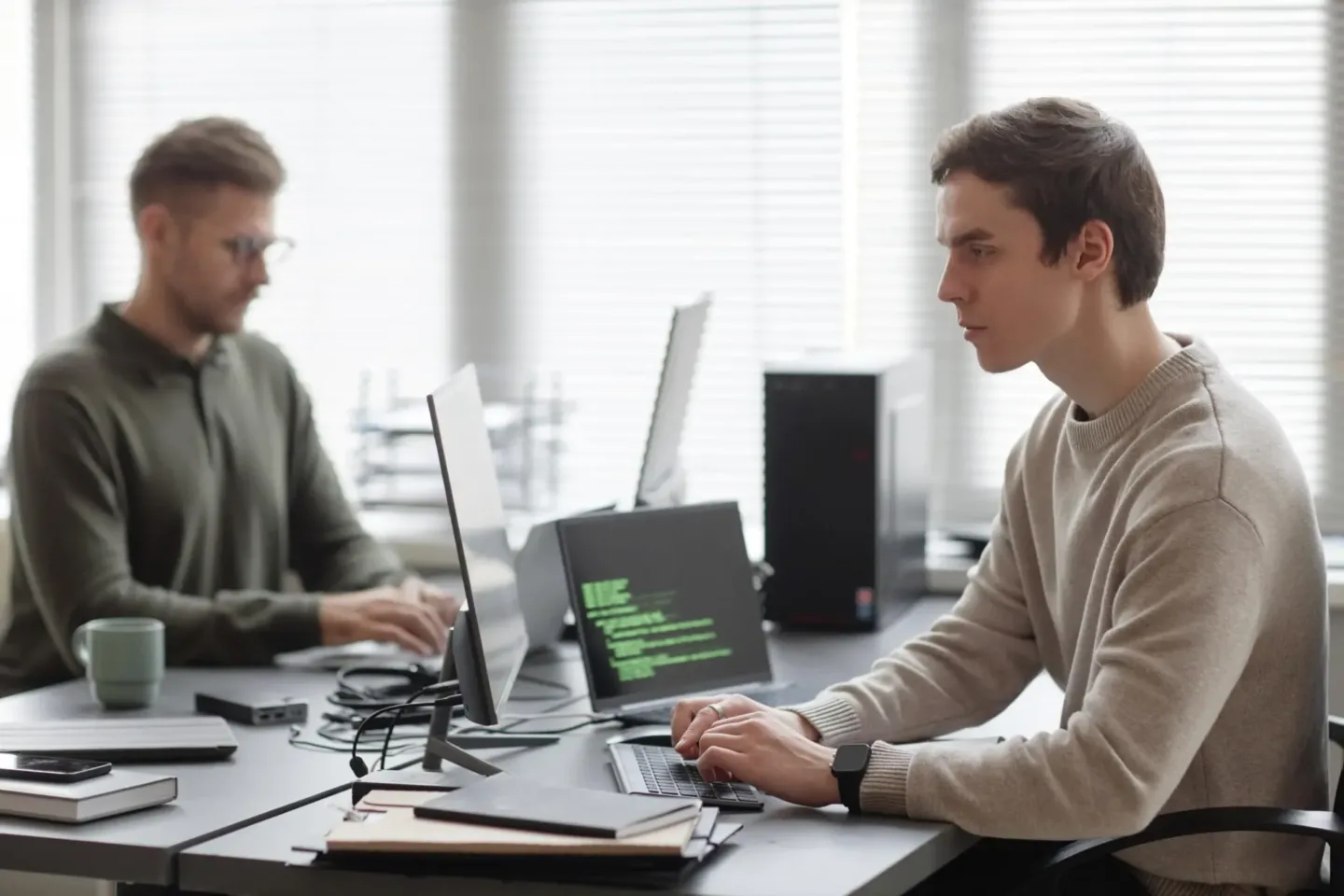 Zwei Männer sitzen gegenüber am Schreibtisch und tippen Code.