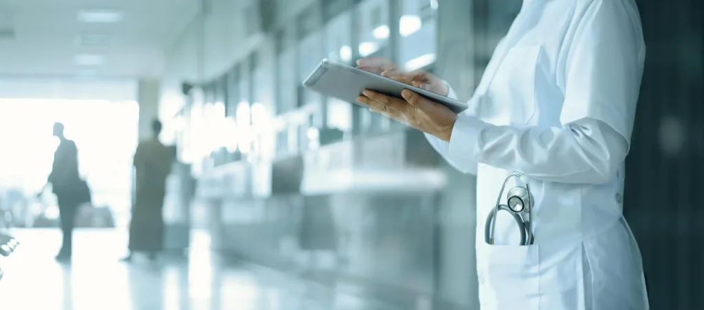 Eine Ärztin steht im Flur des Krankenhauses und bedient ein Tablet.