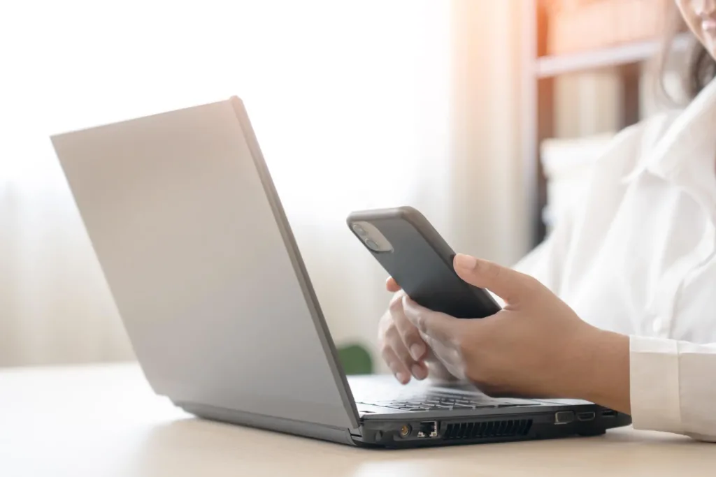 Eine Frau bedient ihr Handy, während sie am Laptop sitzt.